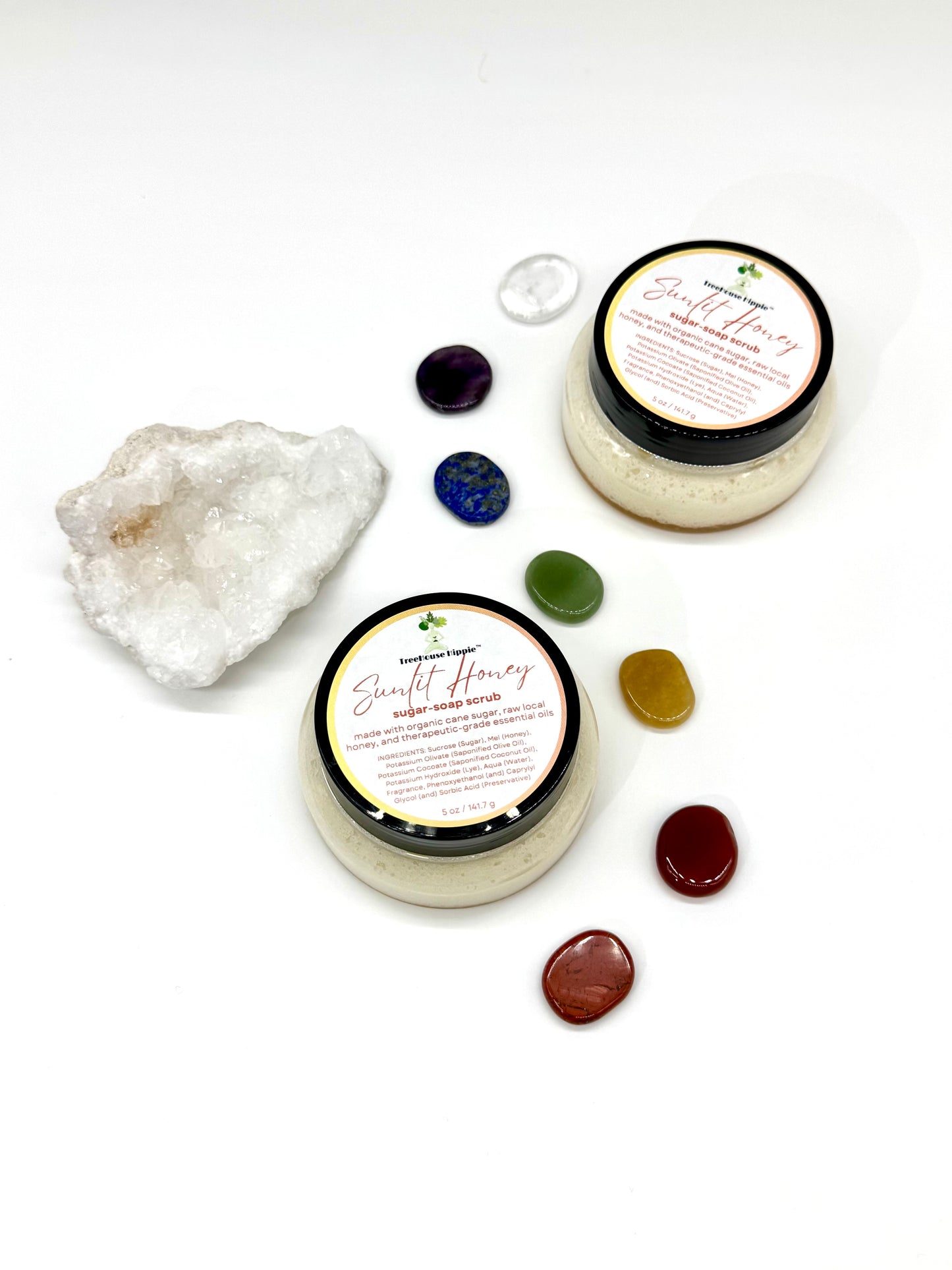 Two of TreeHouse Hippie's ‘Sunlit Honey’ scrubs sitting on a white background with chakra stones and a white quartz crystal. 
