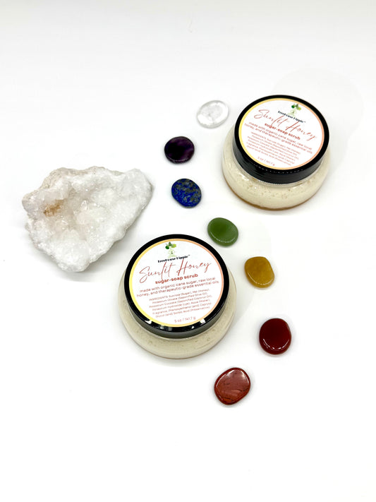 Two of TreeHouse Hippie's ‘Sunlit Honey’ scrubs sitting on a white background with chakra stones and a white quartz crystal. 