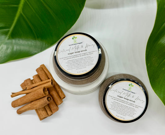 Two of TreeHouse Hippie's 'Oatmeal, Milk, & Honey' scrubs sitting beside cinnamon sticks on a white background with leaf accents.