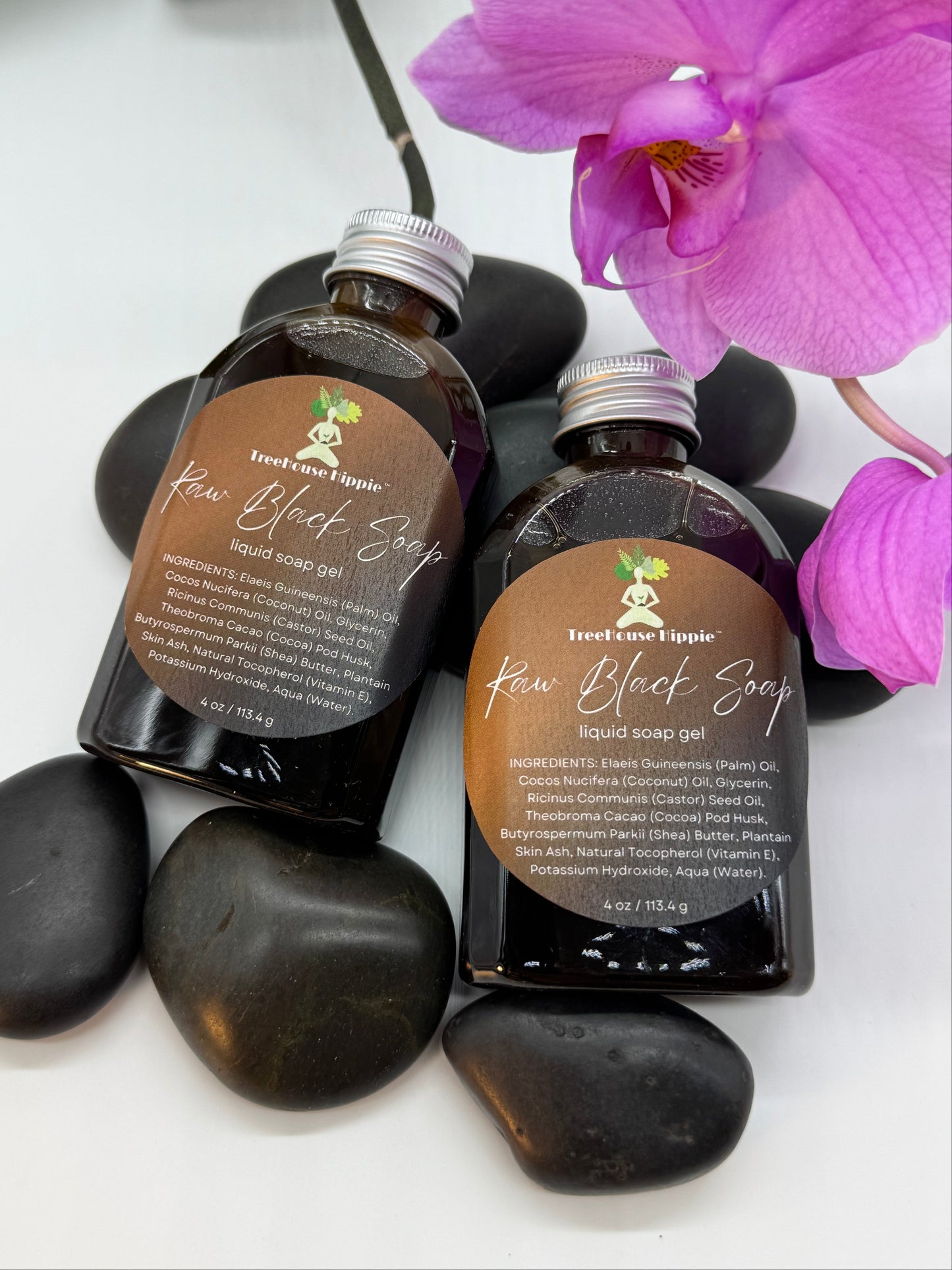 Two small bottles of TreeHouse Hippie's Raw Black Soap Gel with purple orchids and massage stones on a white background. 