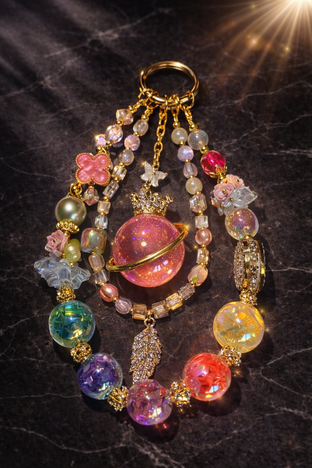 Very colorful decorative keychain with green, yellow, purple, blue, and orange abstract beads, flower accents, a clover bead, and a feather pendant on a dark marble surface. 