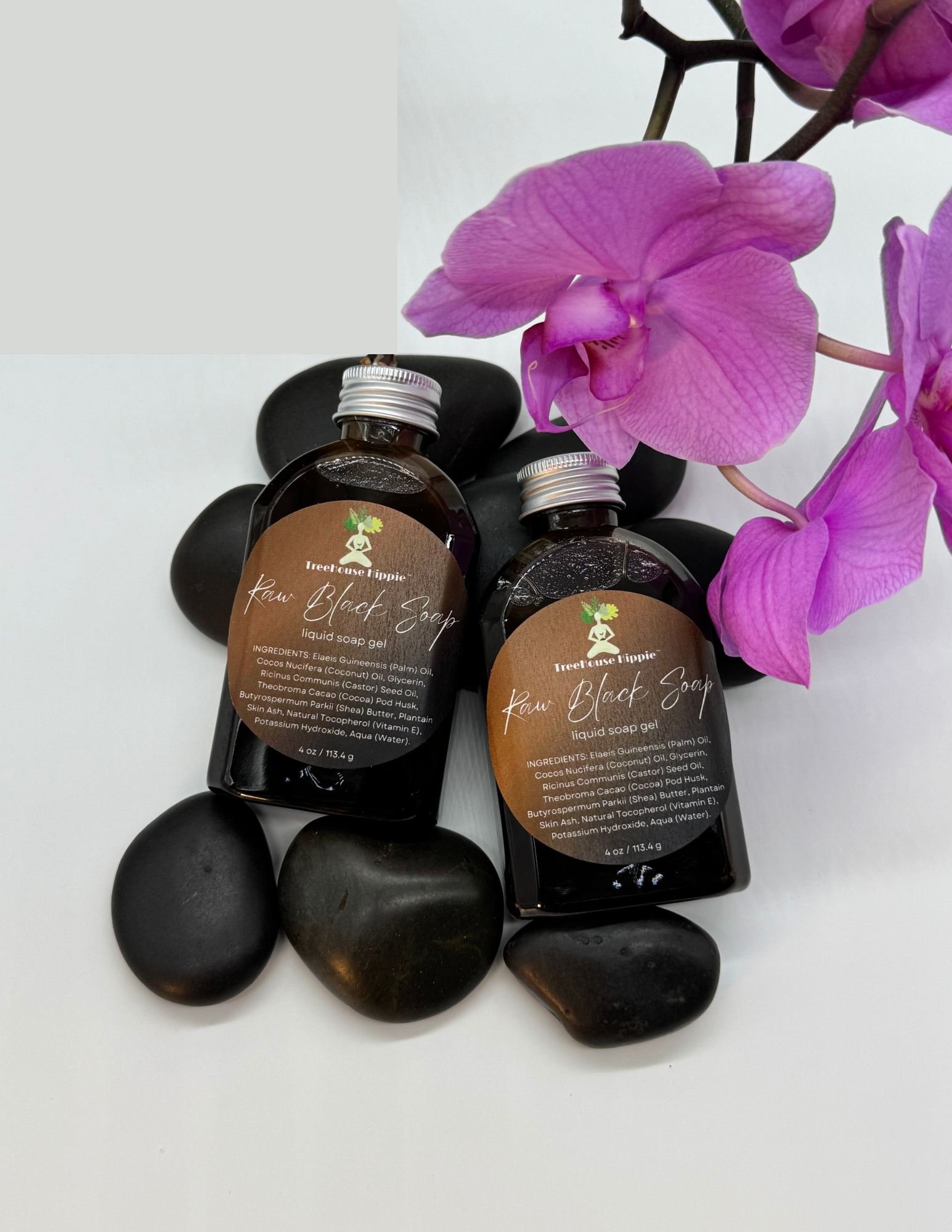 Two small bottles of TreeHouse Hippie's Raw Black Soap Gel with purple orchids and massage stones on a white background. 