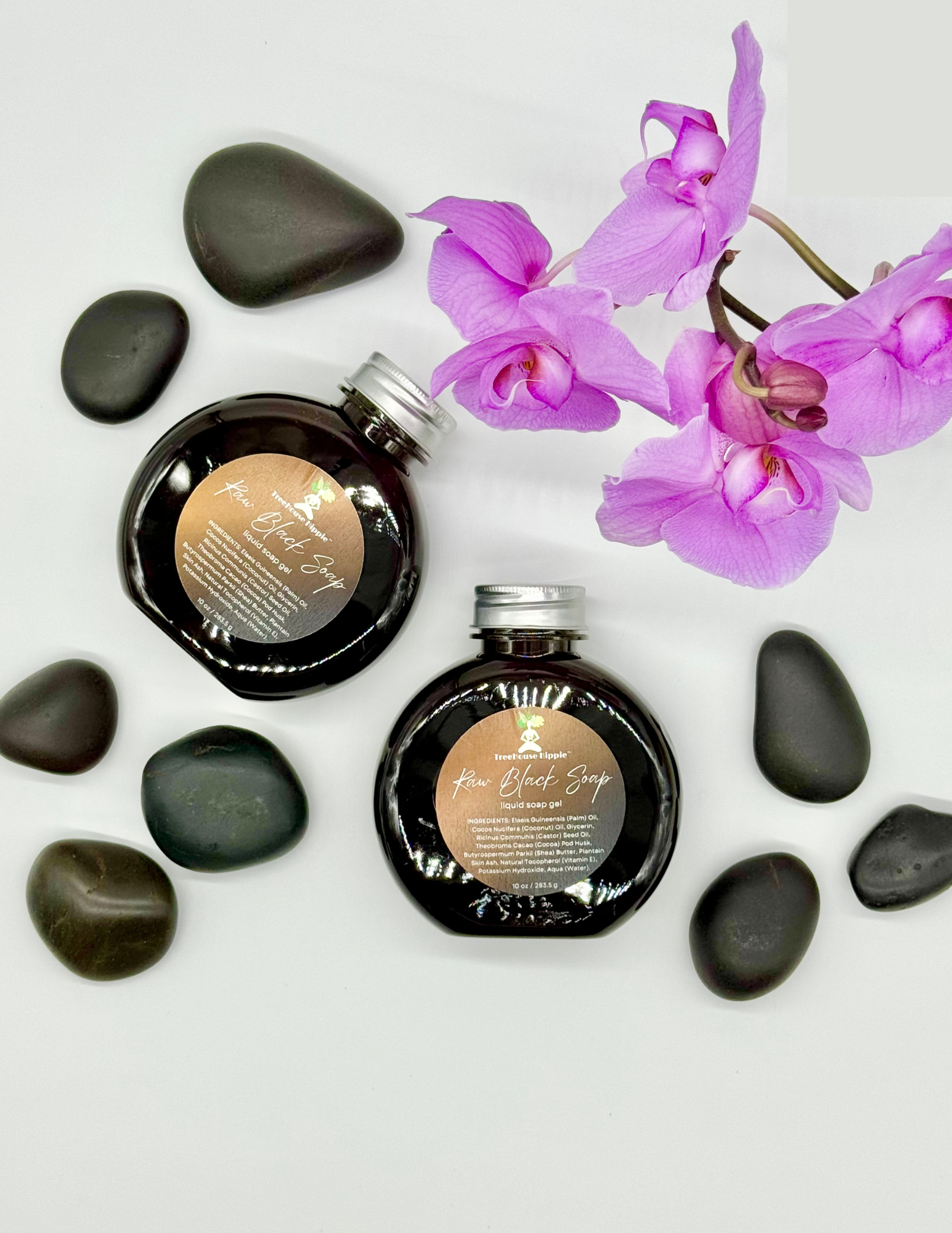 Two large bottles of TreeHouse Hippie's Raw Black Soap Gel with purple orchids and massage stones on a white background. 