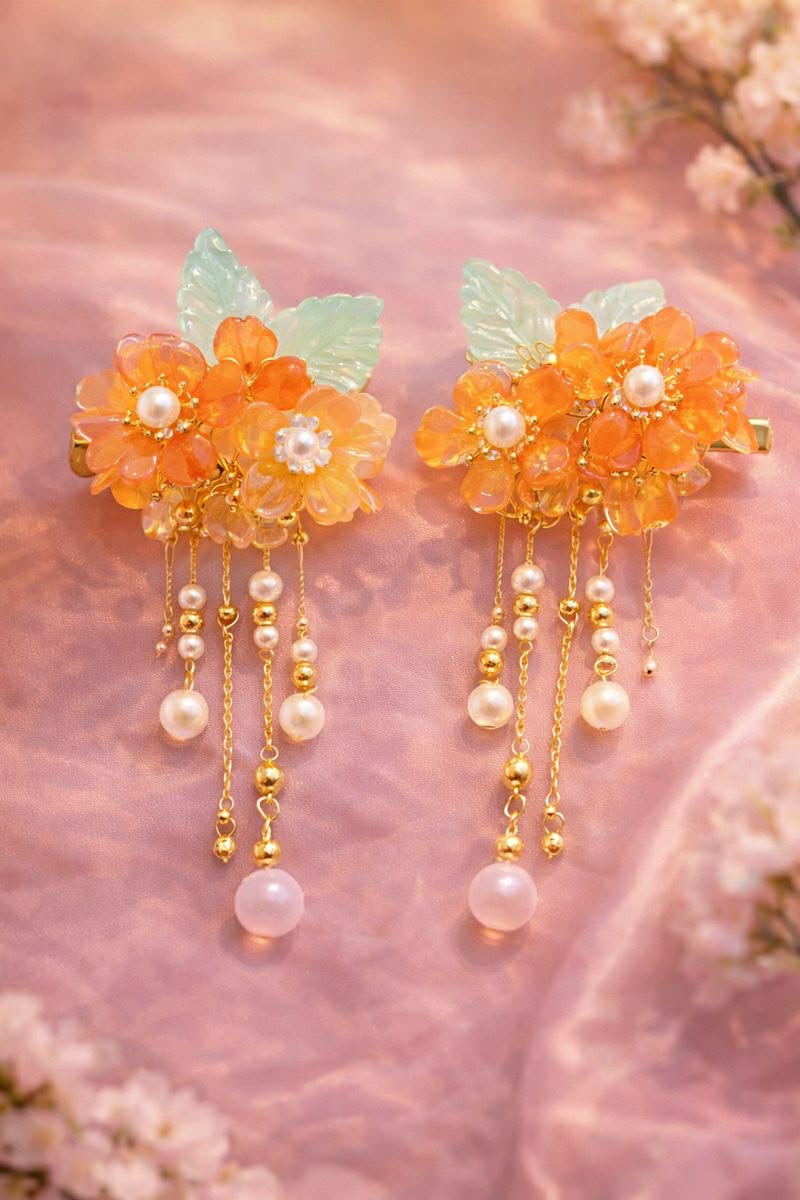 Orange flower hair clips with pearl beaded accents on a soft pink background.