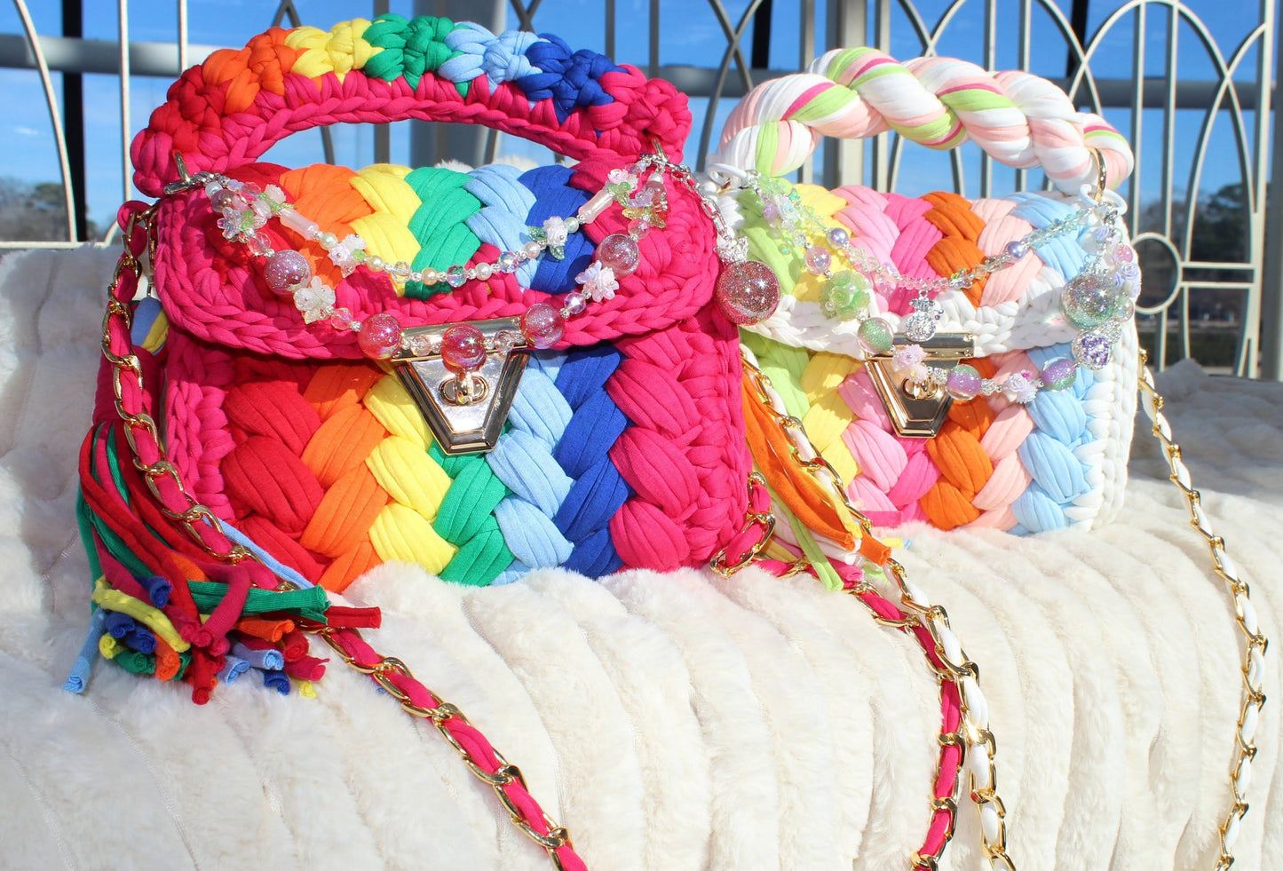 Two colorful Crochet woven handbags with decorative keychains and tassels sitting on White textured surface. 