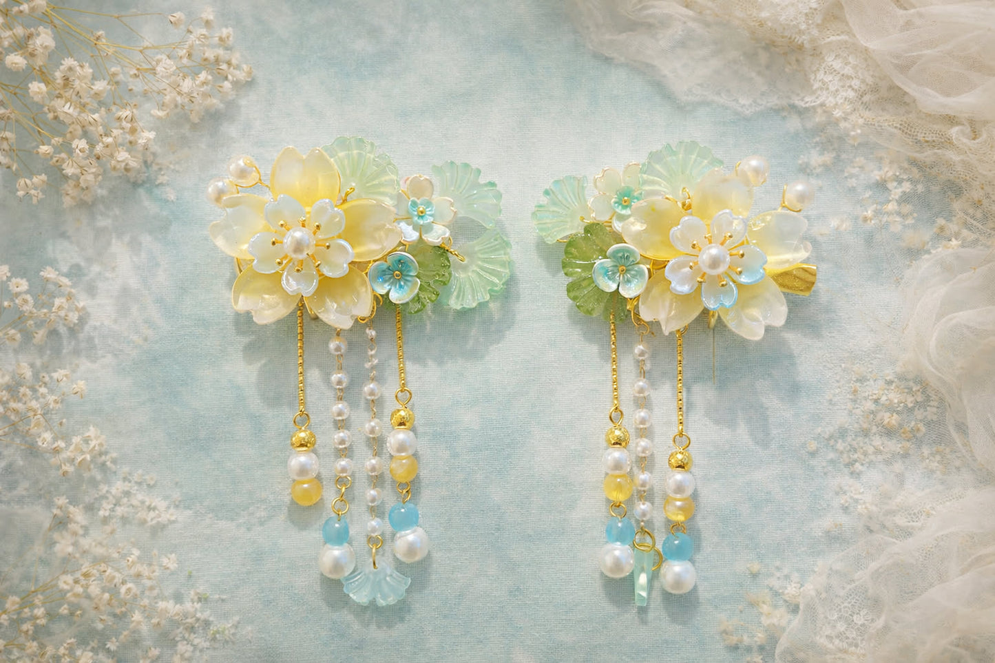 Yellow flower hair clips with pearl beaded accents on a soft mint-green background with white floral decor. 